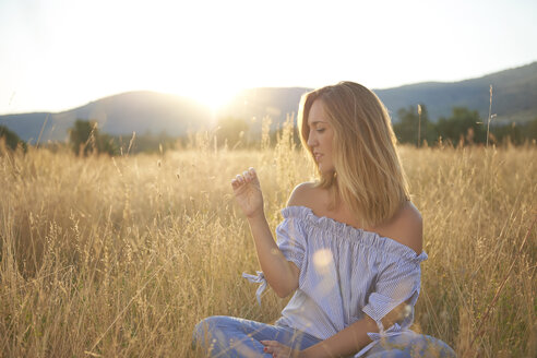 Blond woman sitting on meadow at backlight - JCF00061