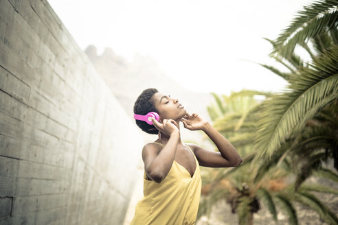Spanien, Frau mit geschlossenen Augen hört Musik mit rosa Kopfhörern - SIPF00972