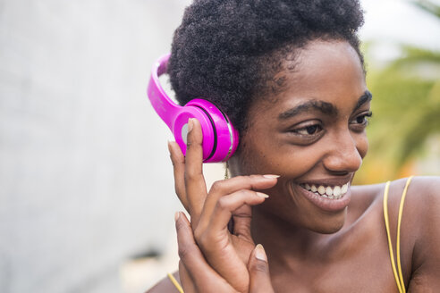 Porträt einer glücklichen Frau, die mit rosa Kopfhörern Musik hört - SIPF00973