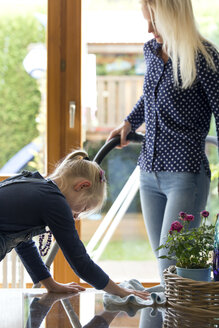Girl cleaning glass table while her mother hoovering - MIDF00795