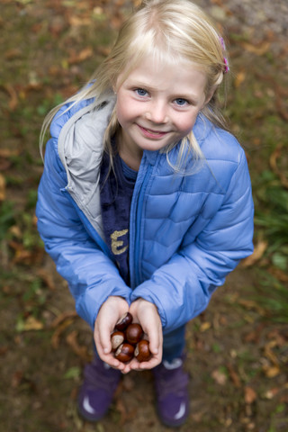Porträt eines lächelnden blonden kleinen Mädchens, das Kastanien in den Händen hält, lizenzfreies Stockfoto