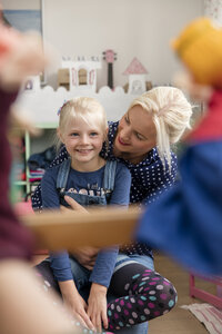 Glückliches kleines Mädchen, das sich zusammen mit seiner Mutter im Kinderzimmer ein Kasperletheater ansieht - MIDF00803