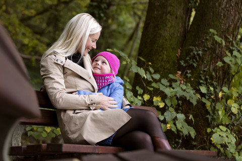 Mutter und kleine Tochter sitzen auf einer Bank im herbstlichen Wald, lizenzfreies Stockfoto