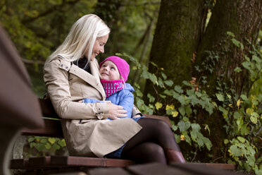 Mother and little daughter sitting on a bench in autumnal forest - MIDF00810