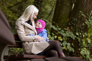 Mutter und kleine Tochter sitzen auf einer Bank im herbstlichen Wald - MIDF00810