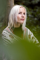 Porträt einer blonden Frau mit Kopftuch, die sich an einen Baumstamm lehnt - MIDF00812