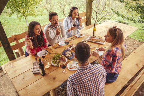 Freunde beim geselligen Beisammensein am Tisch im Freien mit Rotwein und kaltem Snack, lizenzfreies Stockfoto