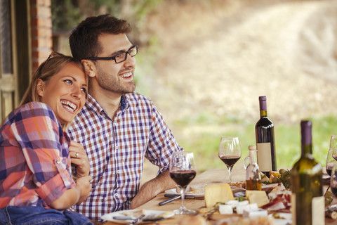 Glückliches Paar am Tisch im Freien mit Rotwein und kaltem Snack, lizenzfreies Stockfoto