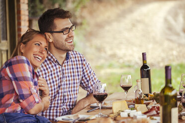 Happy couple at outdoor table with red wine and cold snack - ZEDF00408