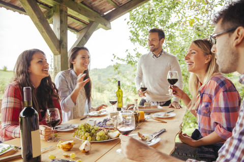 Freunde beim geselligen Beisammensein am Tisch im Freien mit Rotwein und kaltem Snack, lizenzfreies Stockfoto