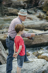 Grandfather and grandson fishing together at rock coast - DAPF00415