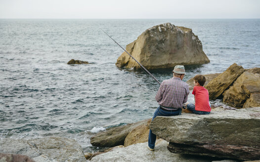 Großvater und Enkel fischen gemeinsam am Meer auf einem Felsen sitzend - DAPF00424