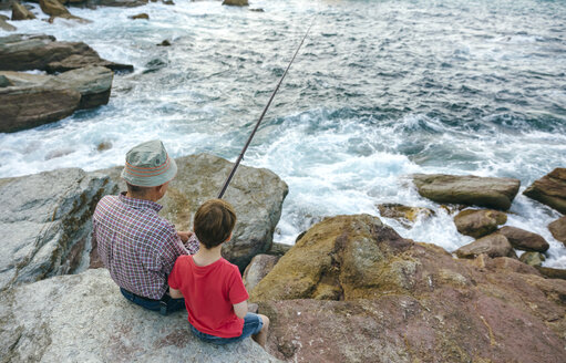 Großvater und Enkel fischen gemeinsam am Meer auf einem Felsen sitzend - DAPF00430