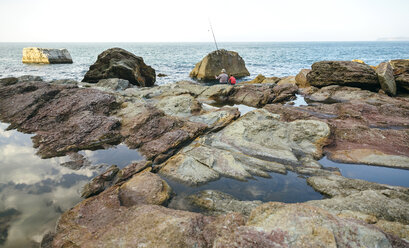 Grandfather and grandson fishing together at the sea sitting on rock - DAPF00431