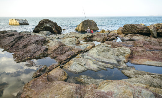 Großvater und Enkel fischen gemeinsam am Meer auf einem Felsen sitzend - DAPF00431