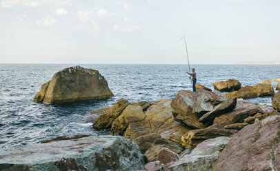 Man fishing while standing on rocks at beach stock photo