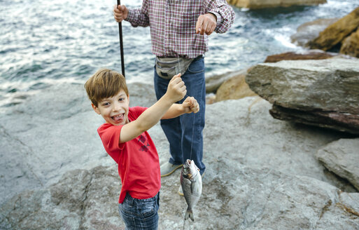 Glücklicher Junge, der einen von seinem Großvater gefangenen Fisch an der Angelschnur hält - DAPF00439