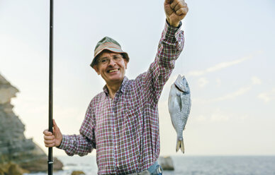 Happy senior man holding fish on fishing line stock photo