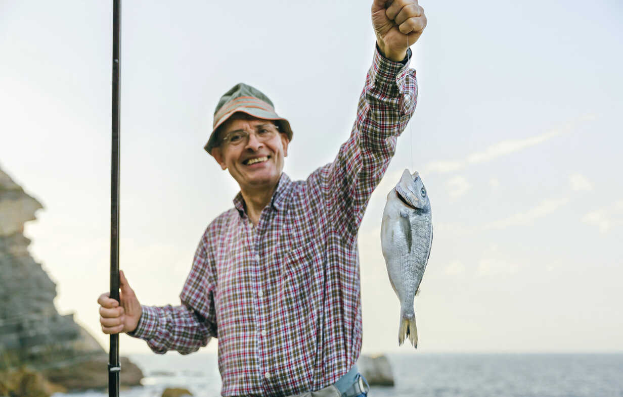 Happy senior man holding fish on fishing line stock photo