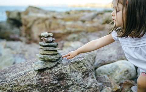 Mädchen mit Steinhaufen an felsiger Küste, lizenzfreies Stockfoto