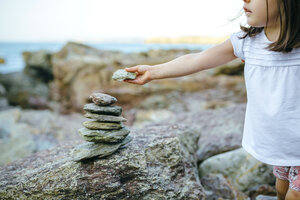 Mädchen stapelt Steine an felsiger Küste - DAPF00448