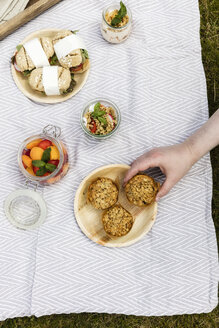 Hand nimmt Muffin von Picknickdecke mit vegetarischen Snacks - EVGF03107