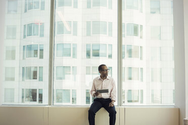 Businessman sitting on window sill holding digital tablet - WESTF21762