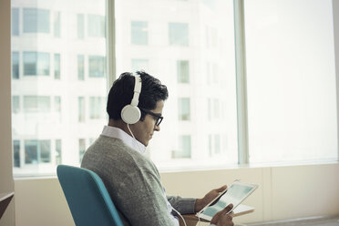 Geschäftsmann, der auf einem Stuhl sitzt, Kopfhörer trägt und ein digitales Tablet benutzt - WESTF21764