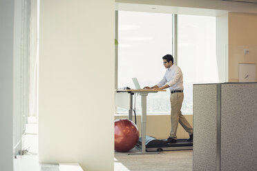 Businessman training on tread mill while using laptop - WESTF21772