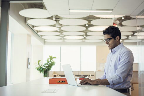 Businessman working at high desk using laptop - WESTF21775