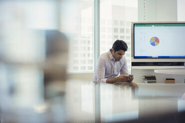 Businessman sitting in office next to screen, checking text messages - WESTF21785