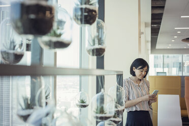 Businesswoman standing in office using smart phone - WESTF21796