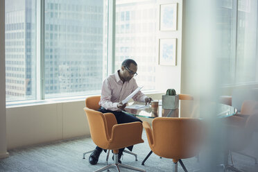 Businessman working alone in office reading documents - WESTF21809