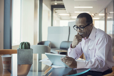 Businessman working alone in office using digital tablet - WESTF21814