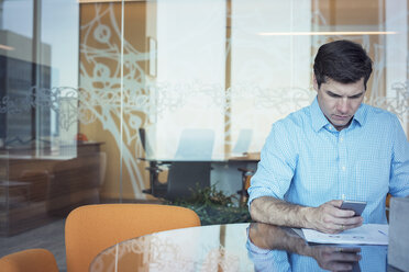 Businessman sitting in office, using smart phone - WESTF21820