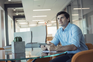 Businessman sitting in office, using digital tablet - WESTF21830