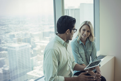 Geschäftsleute mit digitalem Tablet auf der Fensterbank sitzend und diskutierend, lizenzfreies Stockfoto