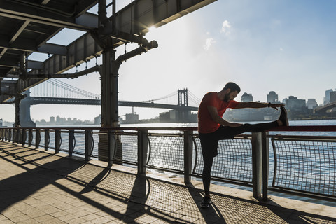 USA, New York City, sportlicher Mann beim Stretching am East River, lizenzfreies Stockfoto