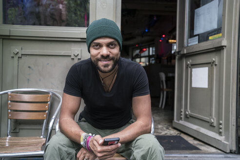 Deutschland, Berlin, Porträt eines lächelnden Mannes, der vor einem Café sitzt - TAMF00701