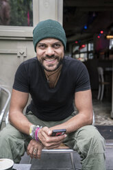 Germany, Berlin, portrait of smiling man siiting in front of coffee shop - TAMF00702