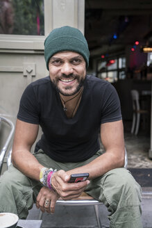 Deutschland, Berlin, Porträt eines lächelnden Mannes, der vor einem Café sitzt - TAMF00702