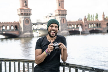 Deutschland, Berlin, Porträt eines glücklichen Mannes mit Kamera vor der Oberbaumbrücke - TAMF00703