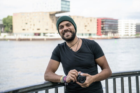 Deutschland, Berlin, Porträt eines glücklichen Mannes mit Kamera - TAMF00706