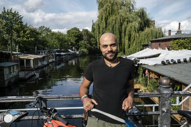 Germany, Berlin, portrait of man with bicycle standing on bridge - TAMF00711