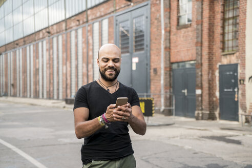 Porträt eines lächelnden Mannes, der auf sein Mobiltelefon schaut - TAMF00716