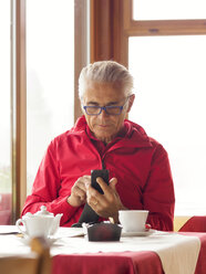 Älterer Mann sitzt in einem Café und benutzt ein Mobiltelefon - LAF01771