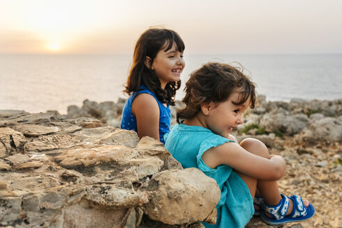 Zwei glückliche kleine Mädchen genießen den Sonnenuntergang am Meer - MGOF02569