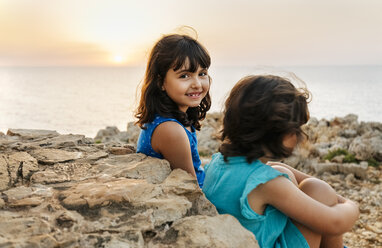 Portrait of happy little girl sitting with her sister near the sea at sunset - MGOF02570