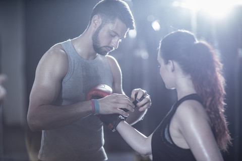 Trainer hilft einer Boxerin beim Anziehen der Boxhandschuhe, lizenzfreies Stockfoto