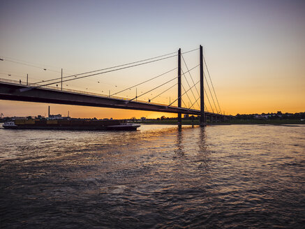 Deutschland, Düsseldorf, Blick auf Rheinknie-Brücke mit Containerschiff auf dem Rhein zur goldenen Stunde - KRPF01909